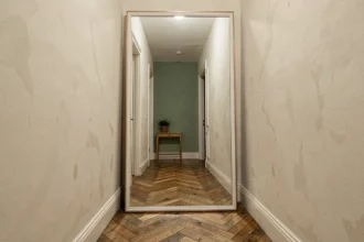 Grand miroir XXL appuyé contre le mur d'un couloir étroit parisien agrandissant visuellement l'espace avec reflet du parquet en chevron