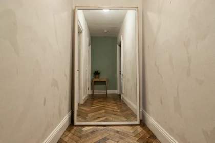 Grand miroir XXL appuyé contre le mur d'un couloir étroit parisien agrandissant visuellement l'espace avec reflet du parquet en chevron
